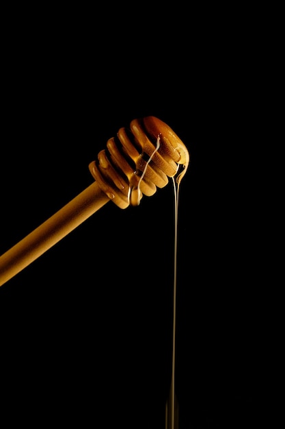 Wooden spoon for honey on black background and liquid fresh honey flowing down it