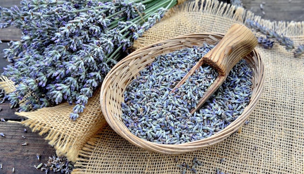 Wooden spoon in a little basket full of petals of lavender flowers on a wooden tablex9