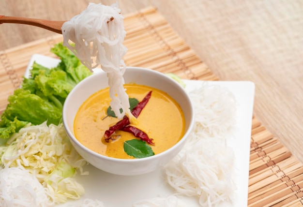 A wooden spoon picking up rice noodles on a white plate on a food and drink background