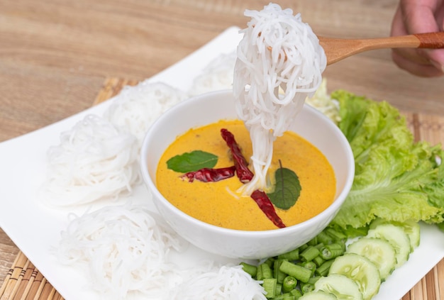 A wooden spoon picking up rice noodles on a white plate on a food and drink background