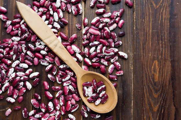 Wooden spoon and violet with dots beans on wooden background.