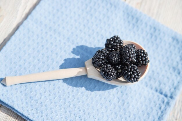 A wooden spoon with blackberries lies on a blue napkin Close up