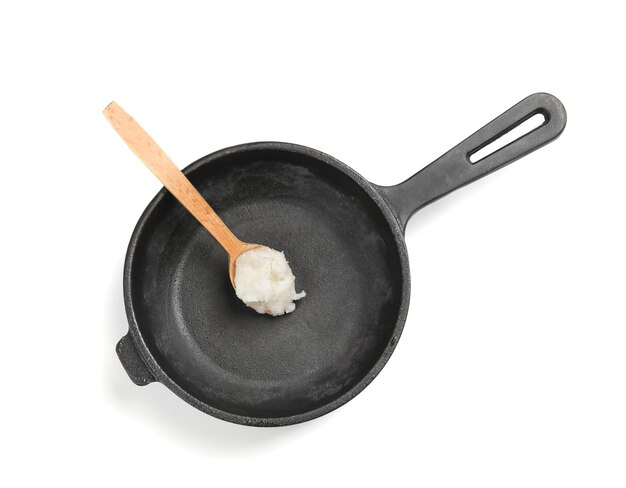 Photo wooden spoon with coconut oil in frying pan on white background