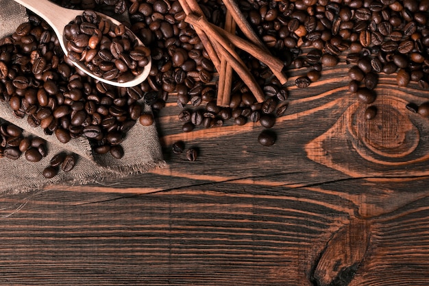 Wooden spoon with coffee beans on wooden table background with cinnamon. Top view. Still life. Copy space. Flat lay.