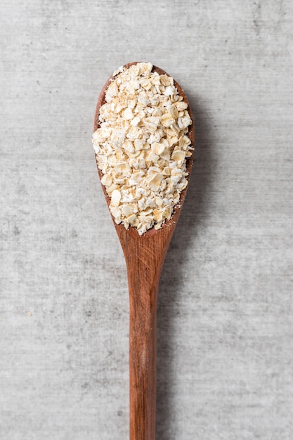 Wooden spoon with oatmeal flakes on a grey wood backrgound. top view. copy space.