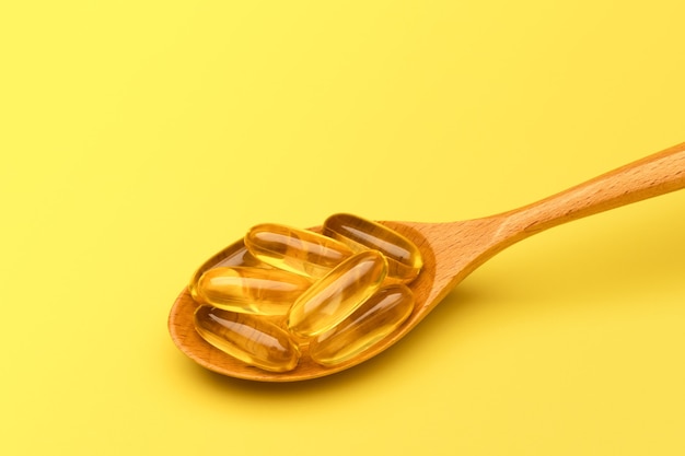 Wooden spoon with Omega 3 pills on yellow surface Copy space