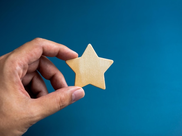 A wooden star in hand isolated on blue background Success and prosperity customer rating quality getting reward concepts