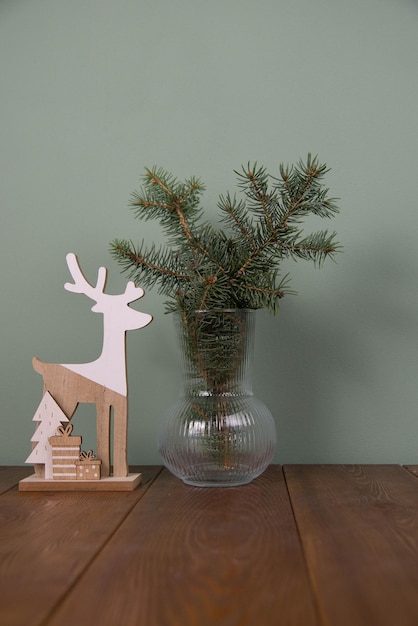 Wooden statuette in the form of a deer and fur branches in vase on green background