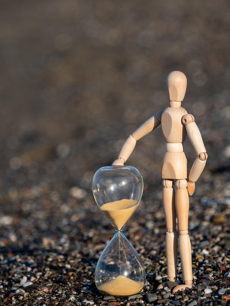 Wooden stick figure next to hourglass on the beach at the seashore