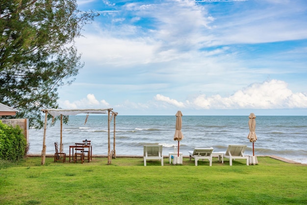 Wooden sun lounger with closed parasol and gazebo on green lawn in tropical sea and blue sky on summer