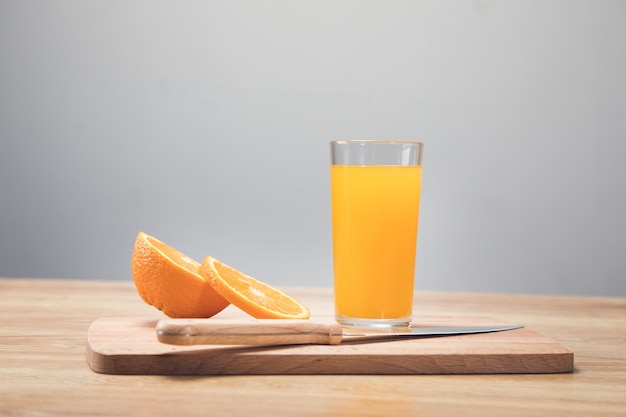 On a wooden table a knife, a glass with a drink and an orange