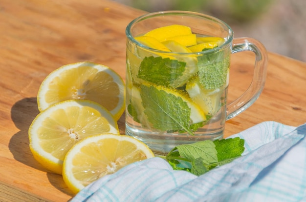 On a wooden table sparkling water with lemon and mint.