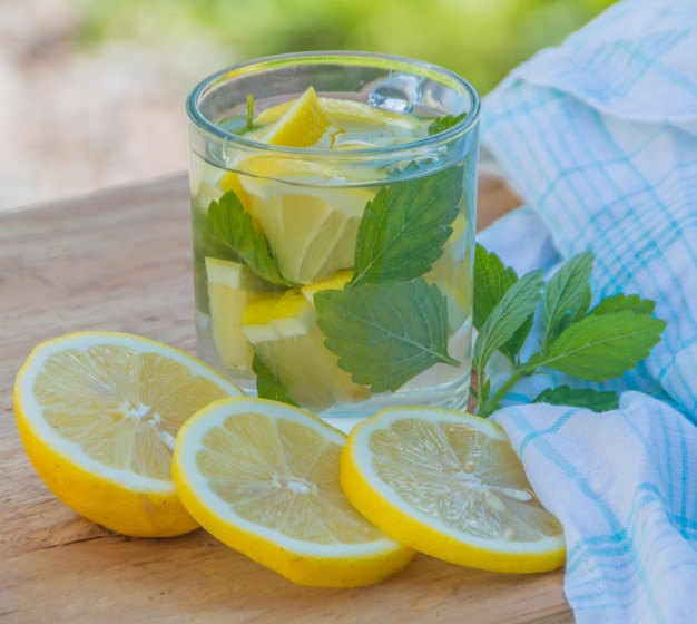 On a wooden table summer drink is water with mint and lemon.