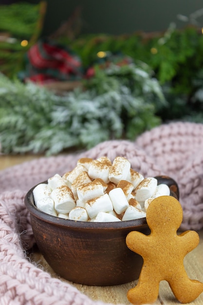 On a wooden table there are two mugs of hot chocolate and marshmallows next to a gingerbread man Christmas card