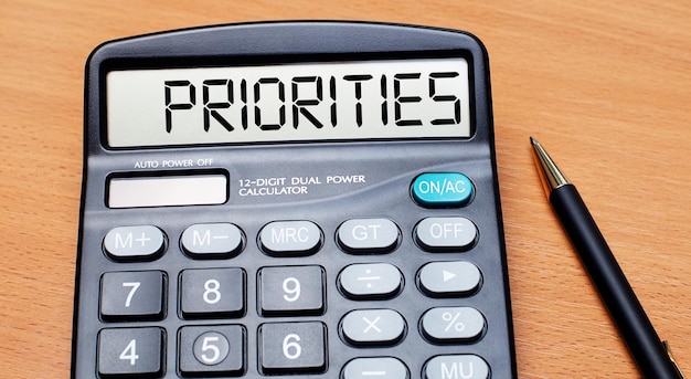 On a wooden table there is a black pen and a calculator with the text PRIORITIES Business concept