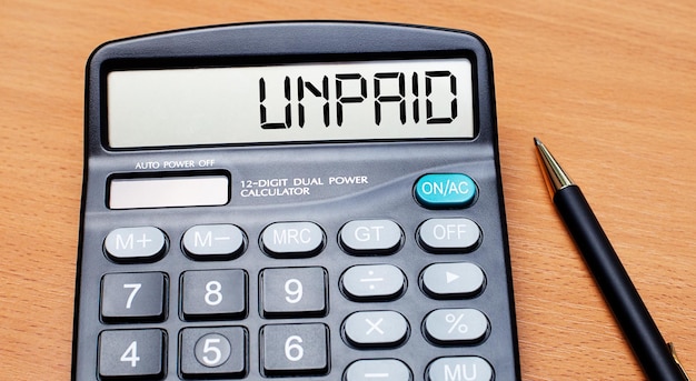 On a wooden table there is a black pen and a calculator with the text UNPAID Business concept