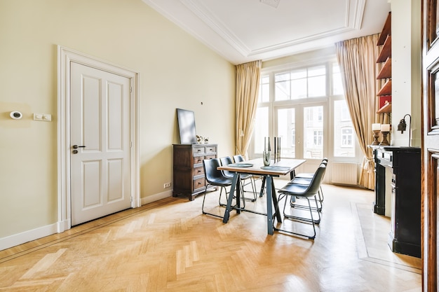 Wooden table with black chairs and decor placed in light room with big windows in elegant curtains