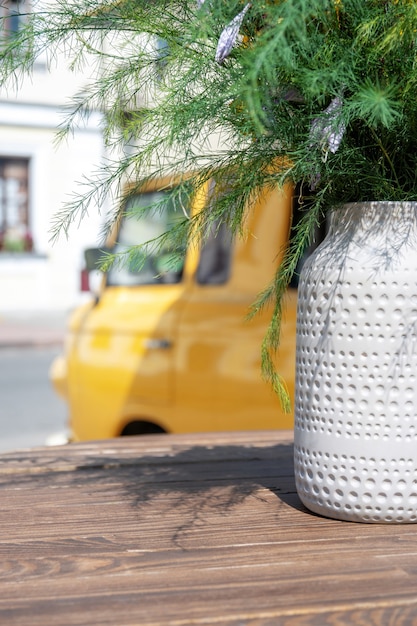 Wooden table with bouquet of flowers in vase on background of yellow van selling coffee.