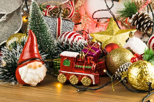 Wooden table with Christmas decorations. Red, silver and gold balls, gift boxes, lights, Santa Claus, Panettone, Christmas tree and others. Selective focus.