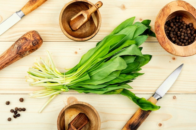 A wooden table with various kitchen tools including a bunch of green leafy greens.