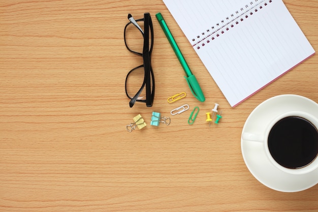 The wooden table working have a coffee mug around a blank book.