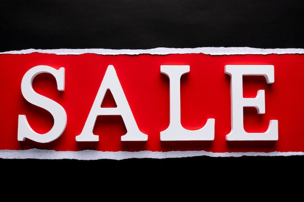 Wooden text  word SALE on black torn and red paper.