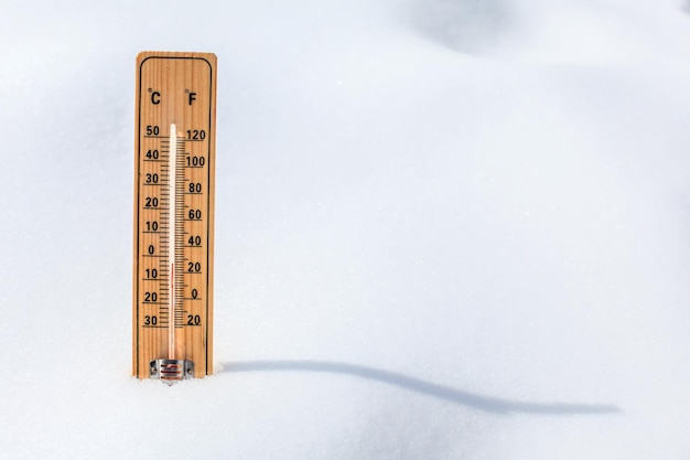 Wooden thermometer standing in snow, showing low temperature, space for text on the right. Winter coming concept.