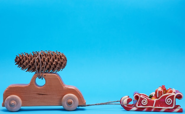 Photo wooden toy car carries on top a pine cone on a blue background