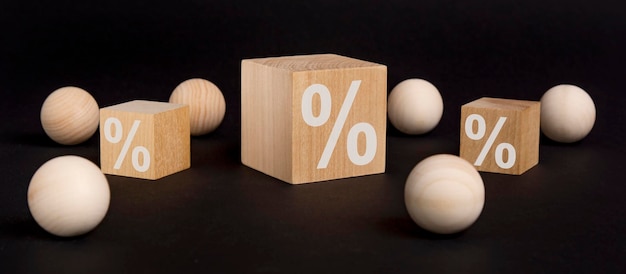 Wooden toy cube with a percent sign viewed high angle on a black background with wooden balls and cubes