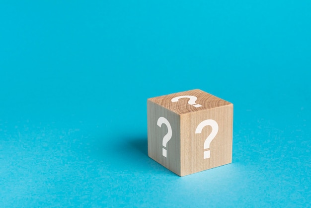 Wooden toy cube with a question mark viewed high angle on a blue background with copy space in a conceptual image