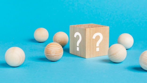 Wooden toy cube with a question marks viewed high angle on a blue background with wooden balls