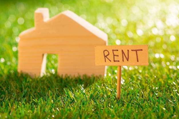 Wooden toy house with rent sign on grass