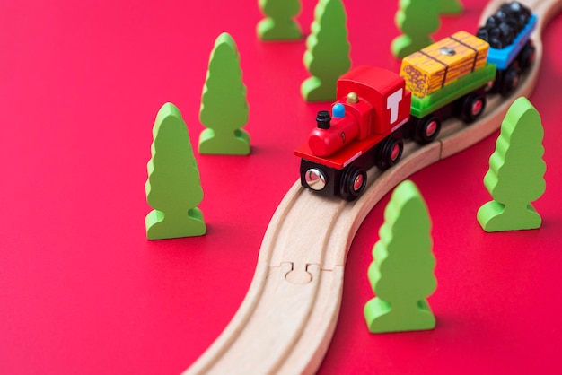 Wooden toy train on the railroad among green trees on red background