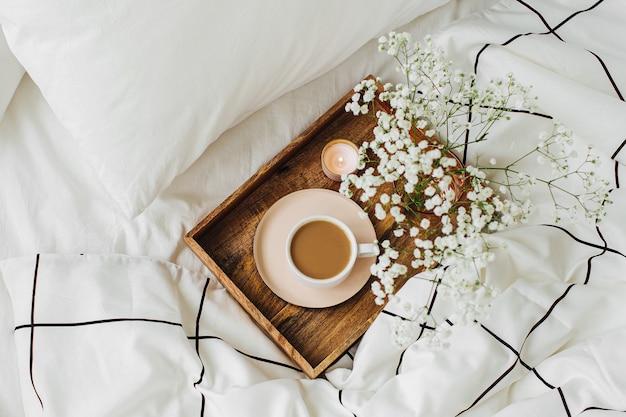 Wooden tray of coffee and candles with flowers on bed. Breakfast in bed. Hygge concept.  