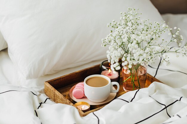 Wooden tray of coffee and candles with flowers on bed.   Breakfast in bed. Hygge concept.