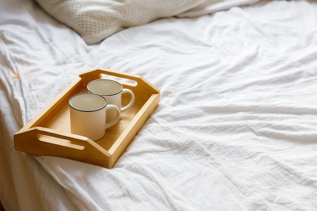 Wooden tray and two white mugs on the bed on a white sheet Cozy morning Coffee in bed