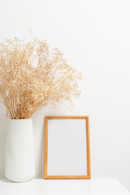 Wooden vertical frame with white vase of gypsophila flowers over white wall