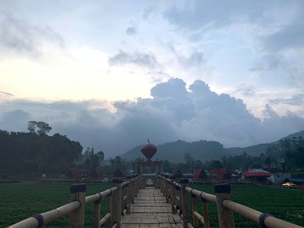 A wooden walkway leads to a field with a building in the background.