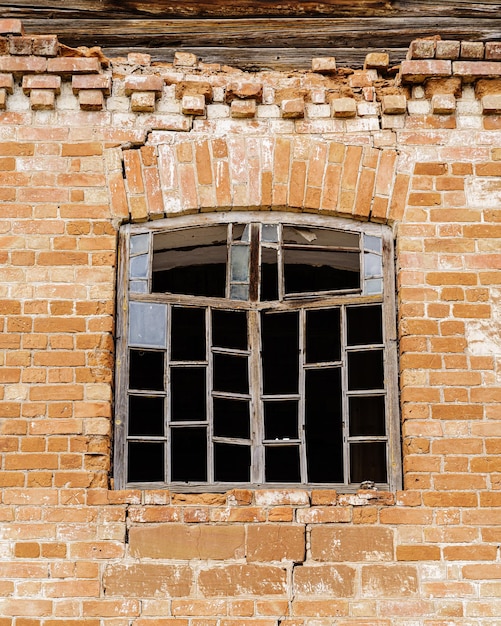 Wooden window frame with broken glass in the wall of an abandoned brick building closeup