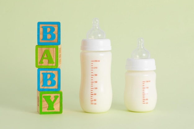 Wooden writing "Baby" next to bottles full of milk on pastel green background