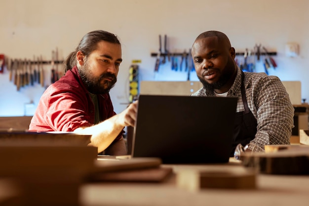 Woodworkers looking over wood processing blueprints on laptop