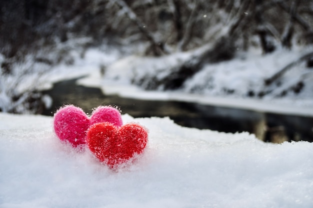 Wool hearts on the white fluffy snow on a winter river shore Love valentines day concept