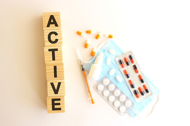 The word ACTIVE is made of wooden cubes on a white background with medical drugs