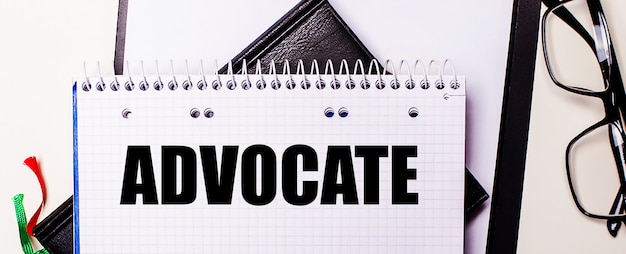 The word ADVOCATE is written in red in a white notebook next to black-framed glasses