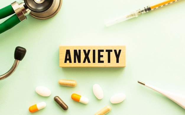 The word anxiety on a wooden cube with a stethoscope and pills medical concept flat lay