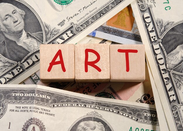 The word ART written in red on wooden cubes over dollar bills