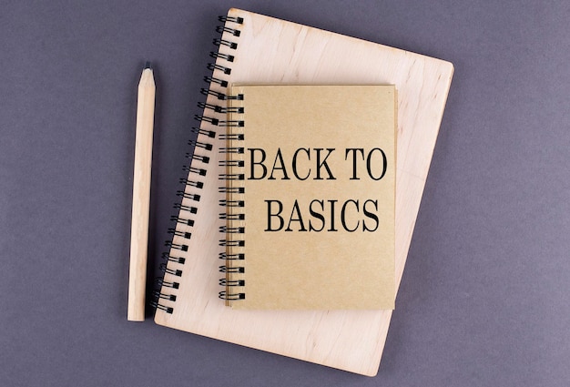 Word BACK TO BASICS on notebook with pencil on the grey background