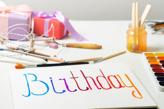 Word Birthday is painted on sheet of paper in watercolors Preparing for holiday with your own hands