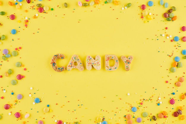 Word candy made of sugar cookies and decorated with small sprinkles on bright yellow background