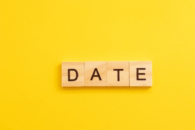 Word DATE made from wooden letters on yellow background.